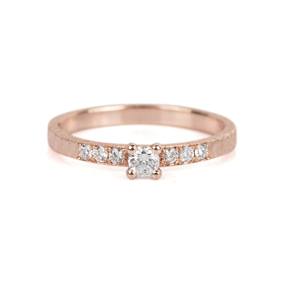Een roodgouden verlovingsring met een diamant en kleine diamantjes op de band