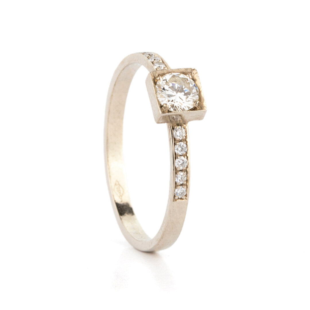 Een witgouden verlovingsring met een diamant in een vierkante zetting en kleine diamantjes op de band