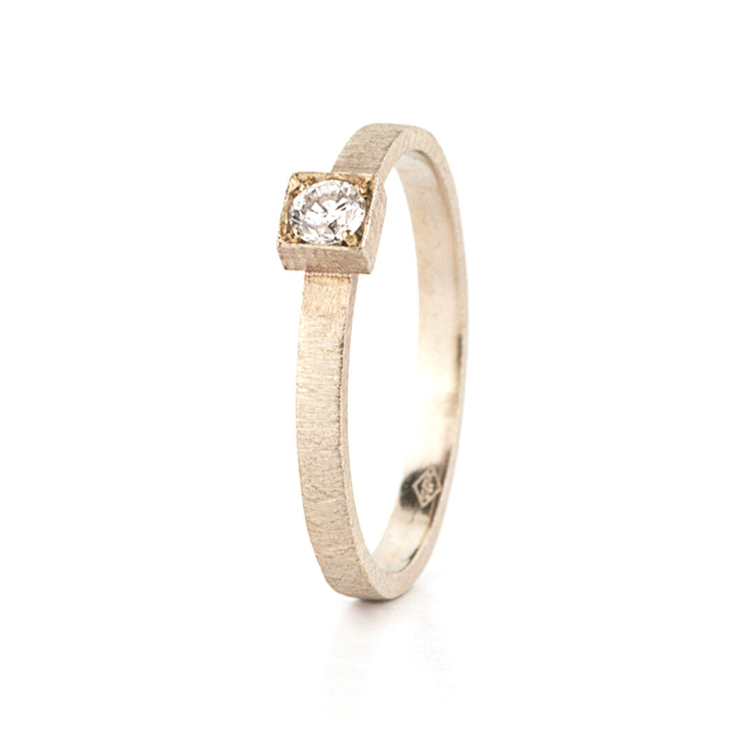 Een geborstelde gouden verlovingsring met een diamant in een vierkante zetting